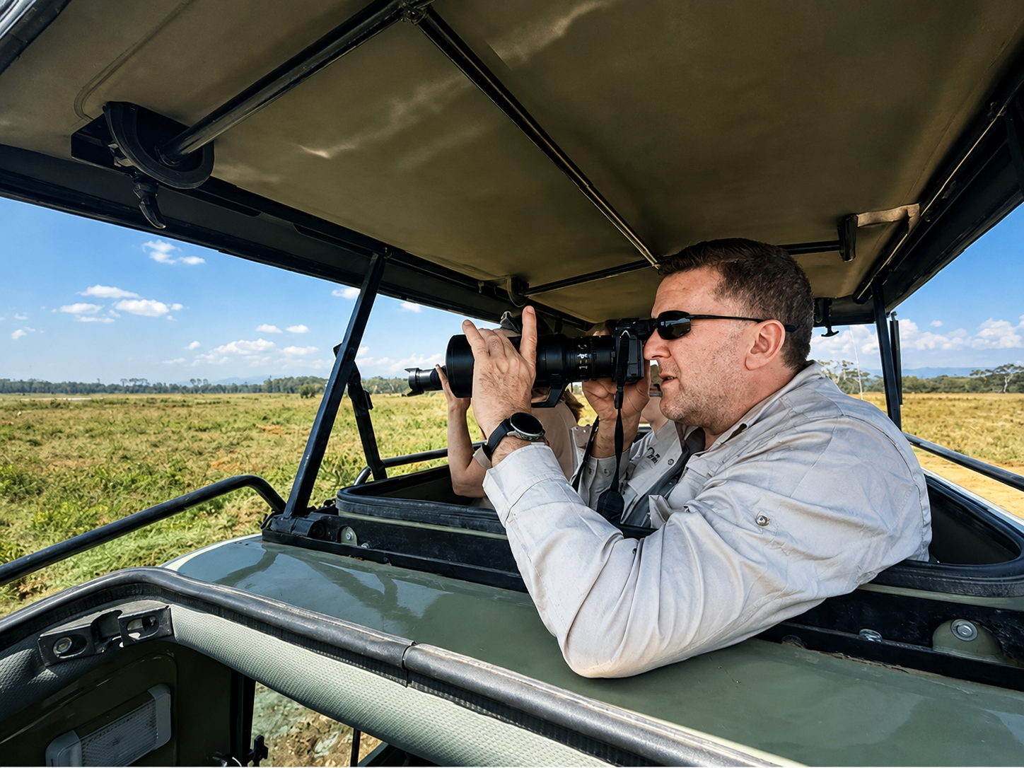 Guest photographing wildlife with a telephoto lens from the roof hatch of a safari vehicle