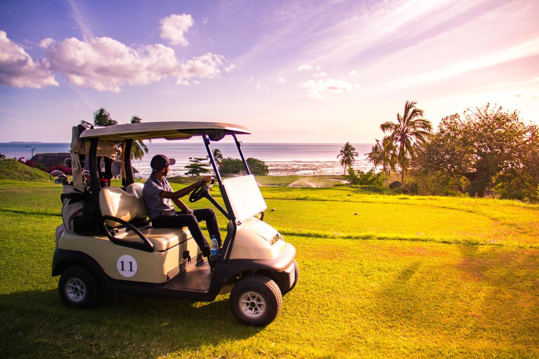 Golf cart driving on course with ocean backdrop at sunset